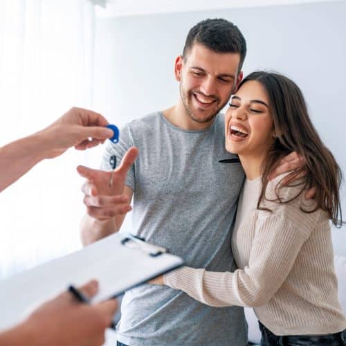 Happy couple is taking keys from their new house from broker and smiling. Hands of estate agent giving keys to the couple. The agent handed the keys a young couple